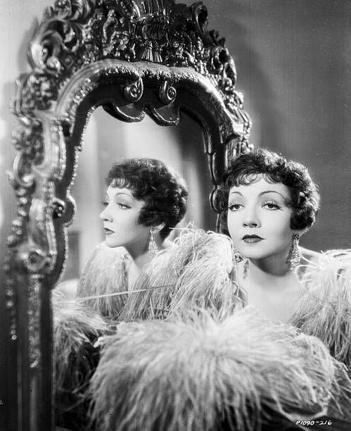 Portrait of actress Claudette Colbert standing next to an ornate